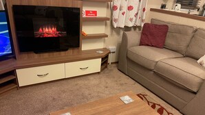 Ein Wohnzimmer mit Fernseher, einer Couch, einem Couchtisch und einem Kamin.