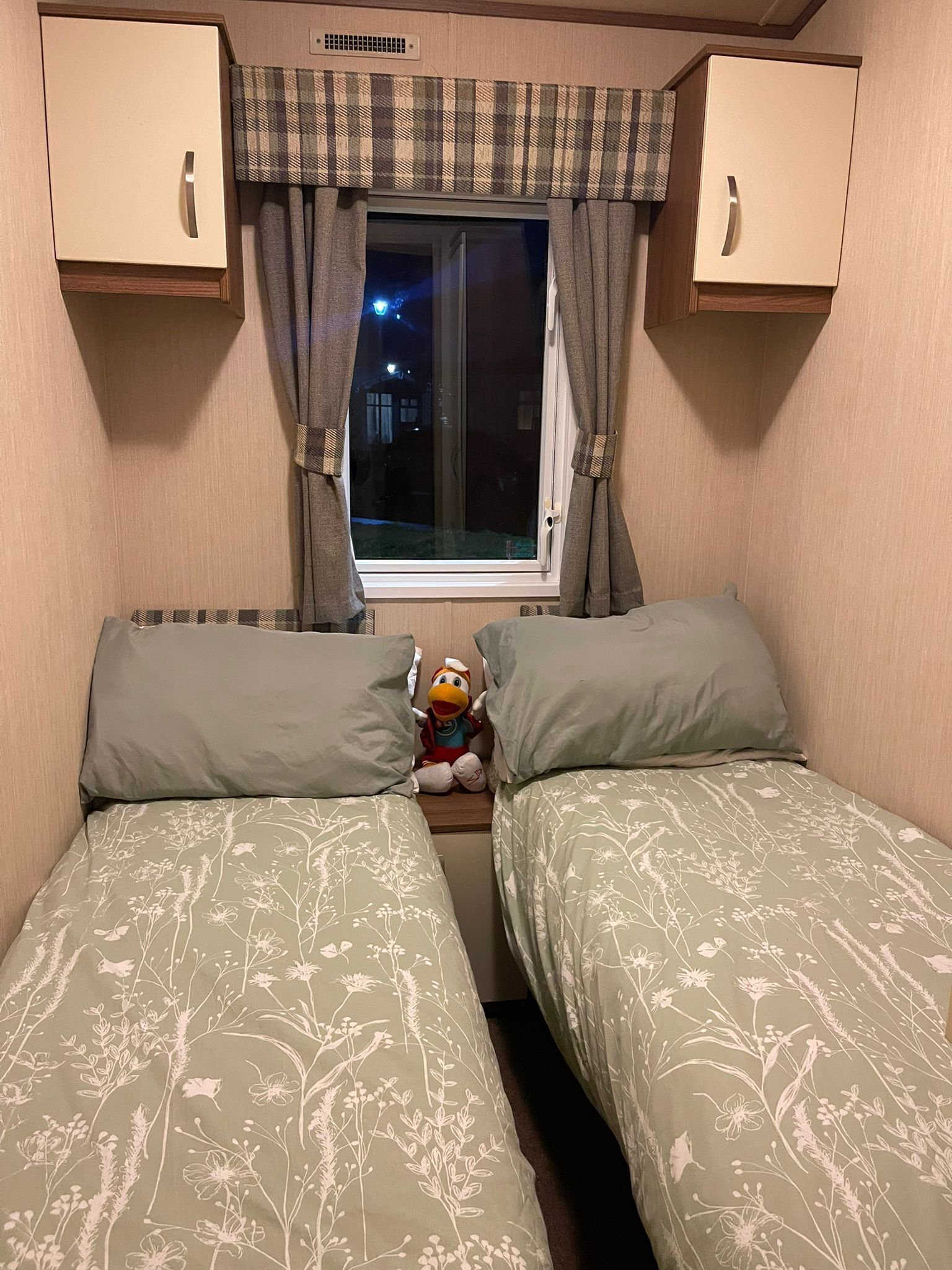 A bedroom with two beds, a window with curtains, and a plush toy on the nightstand.