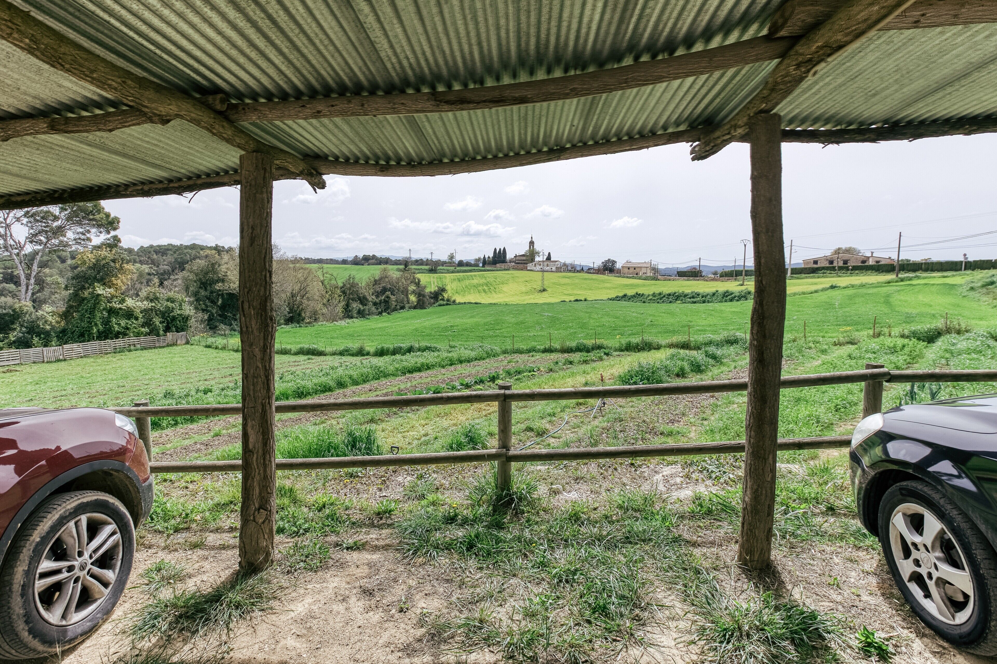 A covered outdoor area with a view of a green field and distant buildings.