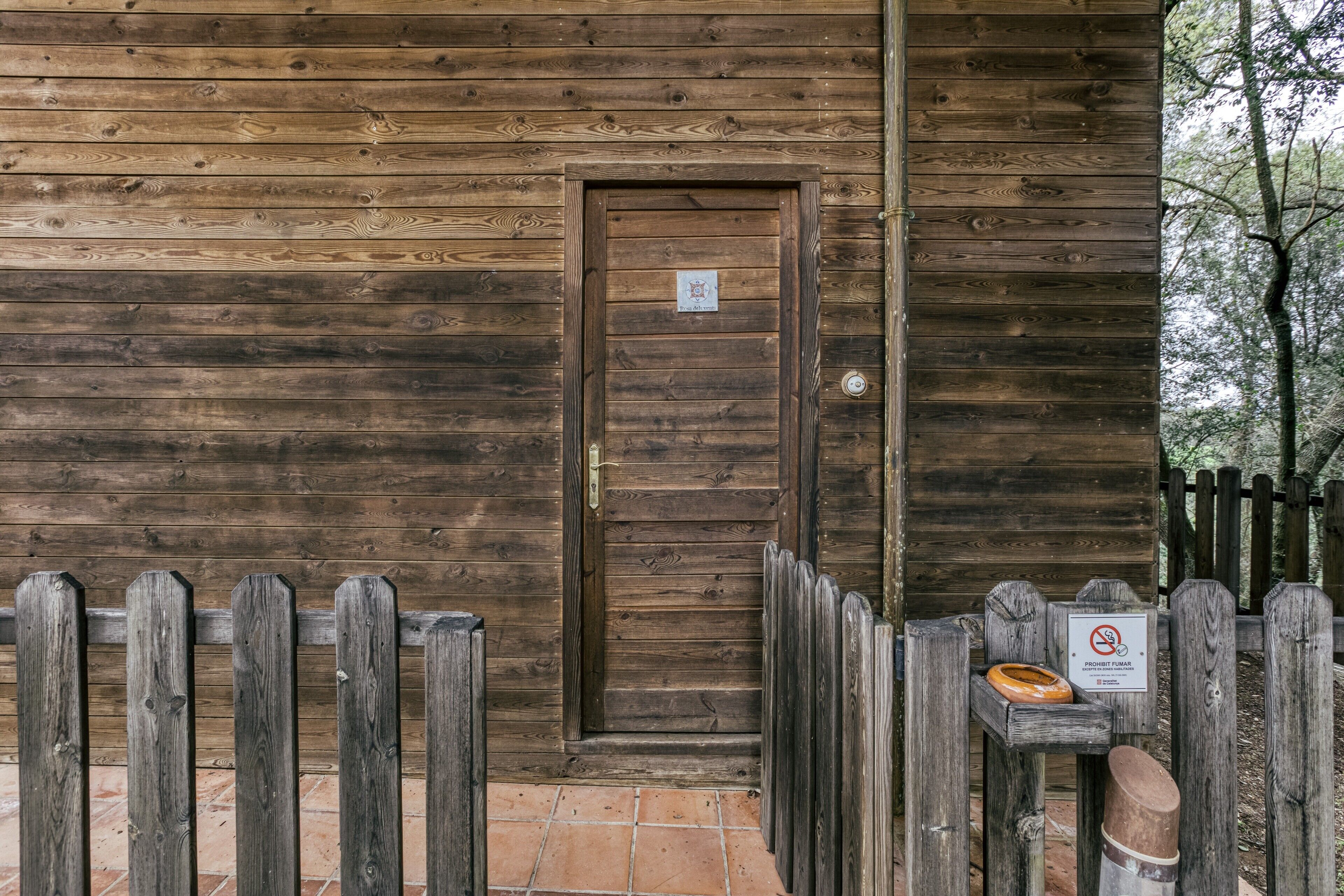 Une cabane en bois avec une porte, une clôture en bois et un panneau indiquant qu’il est interdit d’y entrer avec des chiens.