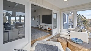 Ett rymligt vardagsrum med en stor TV, bekväma sittplatser och utsikt över omgivningen.