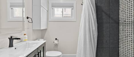 A modern bathroom with a white sink, toilet, and shower curtain.