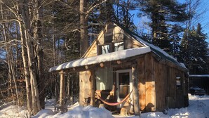 Eine Holzhütte mit Veranda, umgeben von Schnee und Bäumen.