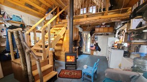 Ein rustikales Blockhaus-Interieur mit einer Holztreppe, einem Kaminofen, einer Küchenzeile und einer gemütlichen Sitzecke.
