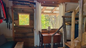 Ein rustikales Holzhaus-Interieur mit einem Holztisch, Stühlen, einer Bank und einem Fenster mit Blick auf viel Grün.