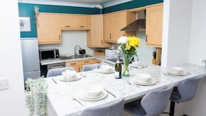 A modern kitchen with wooden cabinets, a marble countertop, and a dining area set for six with grey chairs. - Ramsgate boutique  (Ramsgate)