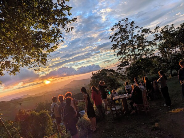 Un groupe de personnes s’est réuni à l’extérieur au coucher du soleil, profitant de la vue sur le paysage et des montagnes lointaines.