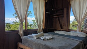 Una habitación de madera con una cama, cortinas y vistas a zonas verdes.