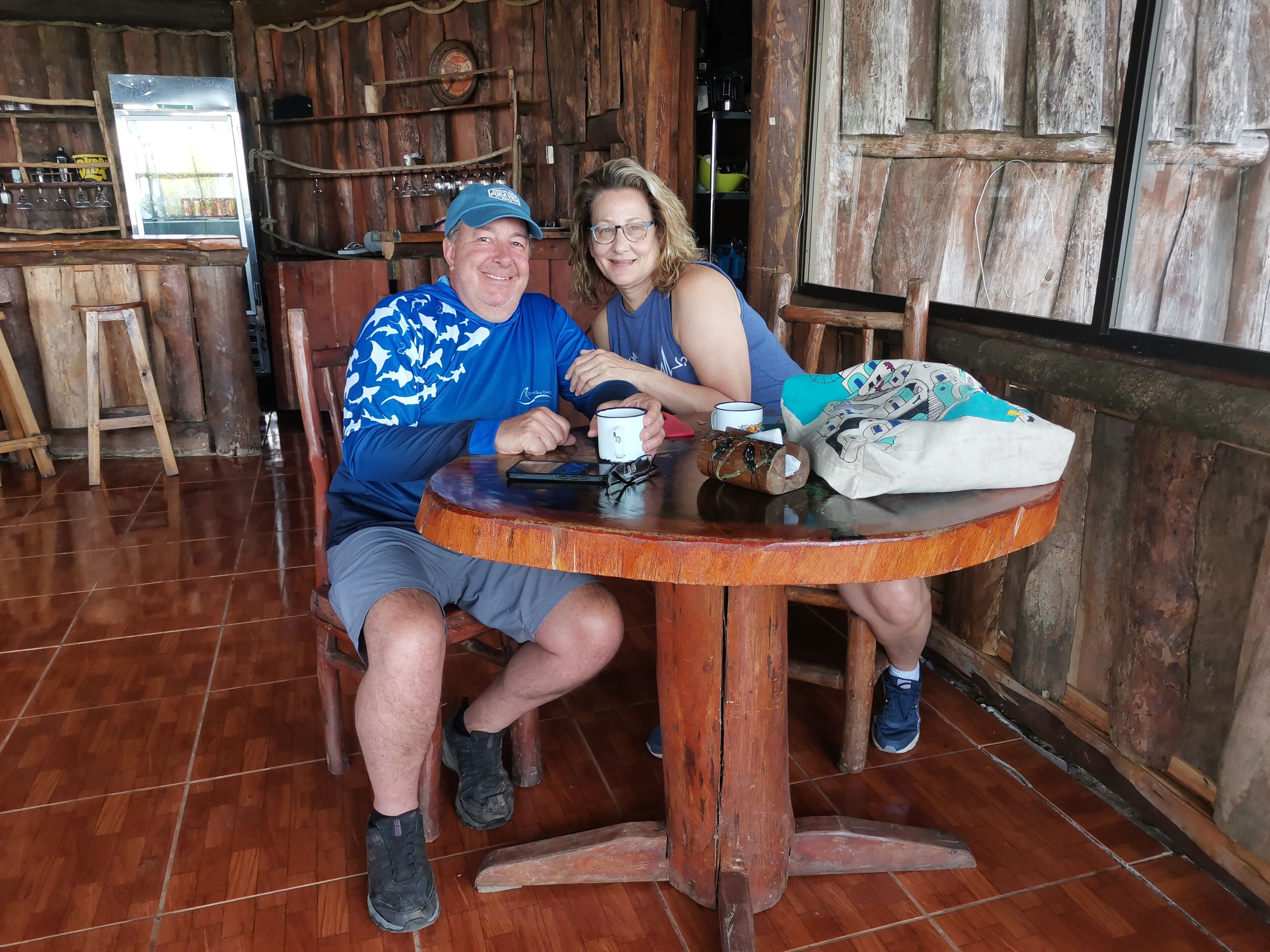 A rustic wooden interior with a round wooden table, chairs, and a refrigerator.