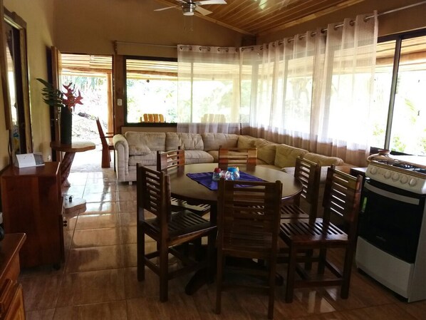 A dining area with a wooden table and chairs, a sofa, and a kitchen with a stove.