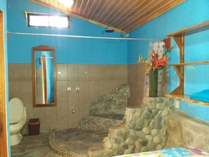 A bathroom with a stone wall, a mirror, a toilet, and a shower area. - Pura Natura Lodge Arroyo (San Lorenzo)