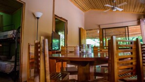 A dining area with a wooden table and chairs, a ceiling fan, and a view of greenery outside.