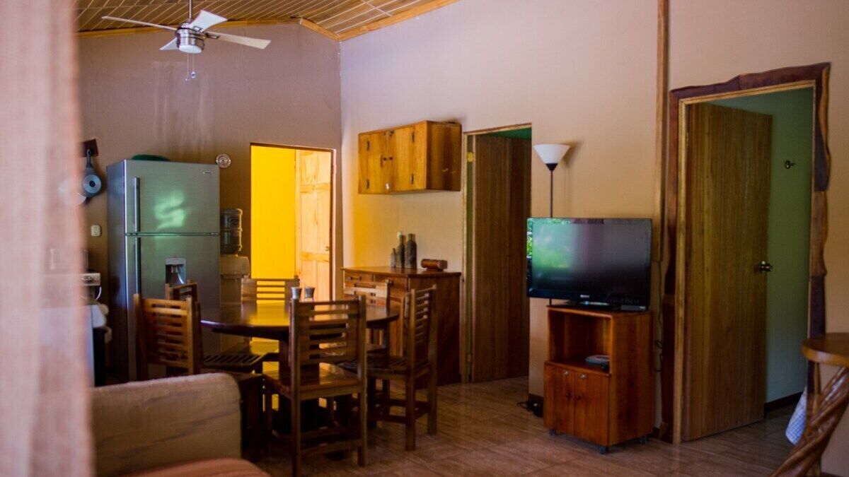 Un espace de vie compact comprenant un coin repas, un téléviseur et des meubles de rangement en bois.