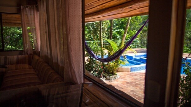 A room with a view of a pool and hammock outside.