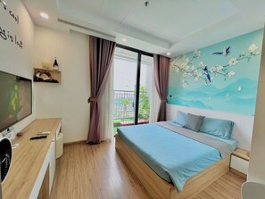 A modern bedroom with a large bed, a desk with a TV, and a balcony with curtains.