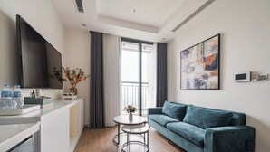 A modern living room with a sofa, a small round table, a flat-screen TV, and a large abstract painting on the wall. - Sunny - Vinhomes GreenBay Residences (Hanoi)