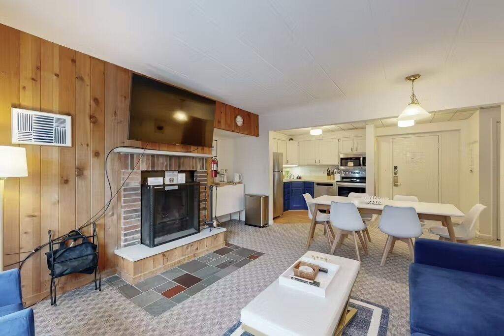 A modern living room with a fireplace, a dining area, and a kitchen.