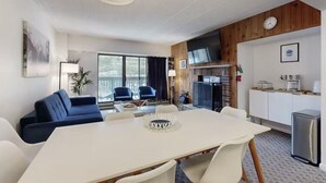 A modern room with a dining table, blue sofa, and a kitchen area with a refrigerator and microwave. - Killington Sapphire (Killington)