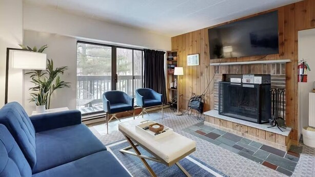 A modern living room with a fireplace, two blue armchairs, a sofa, and a television mounted on the wall. - Killington Sapphire (Killington)