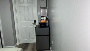 Et lille køleskab med sort håndtag, en Scott Comfort Plus vaskemiddeldispenser, og en blå flaske ovenpå.