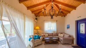 A cozy living room with a wooden ceiling, a chandelier, a sofa set, a coffee table, and a blue door.