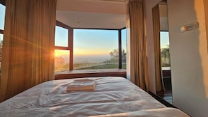 Ein Schlafzimmer mit einem großen Fenster, einem Bett mit weißer Bettdecke und Vorhängen.