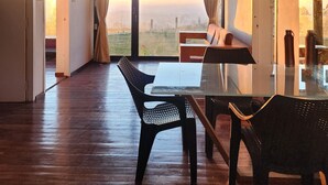 Ein geräumiger Raum mit einem großen Tisch und Stühlen, Blick ins Freie durch ein großes Fenster und einer Deckenleuchte.