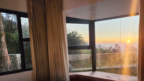 Ein Schlafzimmer mit einem großen Bett, einem Fenster mit Vorhängen und Blick auf den Sonnenuntergang.