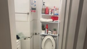 A small bathroom with a toilet, a shelf with toiletries, and a trash bin. - Charming 1-bedroom in a private house in Queens with AC, WiFi. Enjoy your stay (Queens)