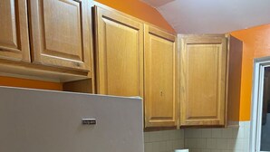 A kitchen with wooden cabinets, a white refrigerator, a microwave, and a window with blinds. - Charming 1-bedroom in a private house in Queens with AC, WiFi. Enjoy your stay (Queens)