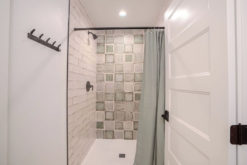 A shower area with a tiled wall, a showerhead, and a curtain.