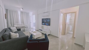 A modern living room with a grey sofa, a coffee table, and a TV mounted on the wall. - 154 LCA - Stay Local Apartment (Larnaca)