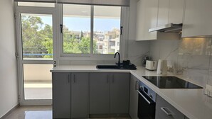 A modern kitchen with a built-in oven, a sink, and a window overlooking a residential area. - 154 LCA - Stay Local Apartment (Larnaca)