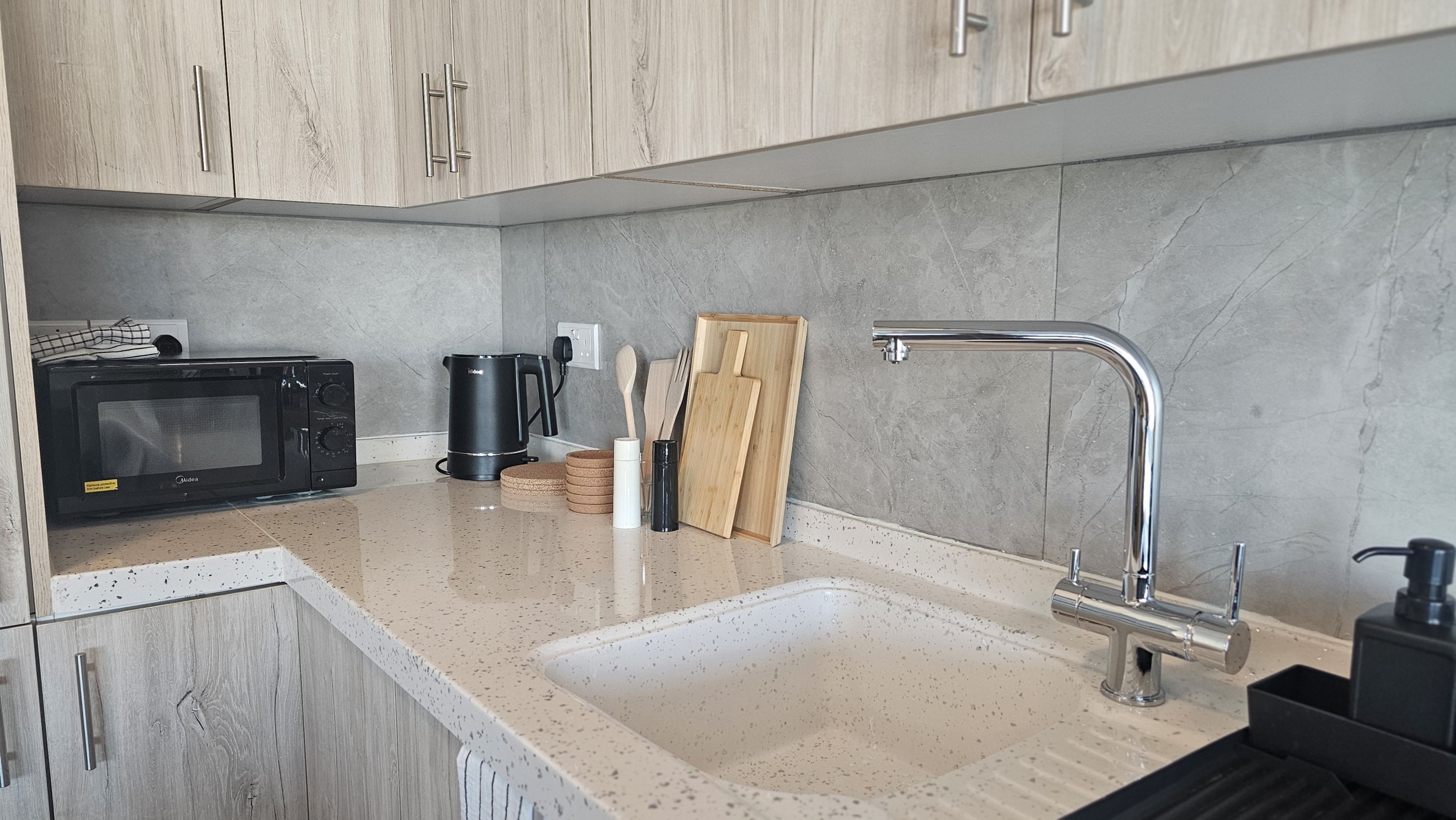 Een moderne keuken met een magnetron, koffiezetapparaat en een houten snijplank.