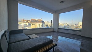 En balkong med en soffa och en bänk, stora fönster med utsikt över staden.