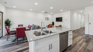 Una cocina moderna con una isla central, pileta de acero inoxidable y muebles color blanco.