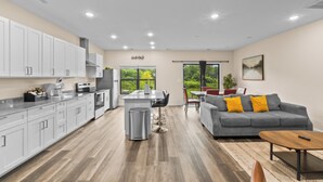 A modern kitchen with white cabinets, a central island, and a dining area with a gray sofa and yellow pillows. - 3BR in Charlotte, 10 Min to Panthers Stadium Pet-Friendly (Charlotte)