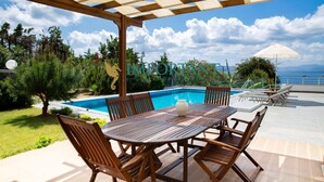 Zona junto a la piscina con una mesa y sillas de madera, una pérgola con vistas a la piscina y un cartel con el nombre 'IMPORTANT GROUP'.