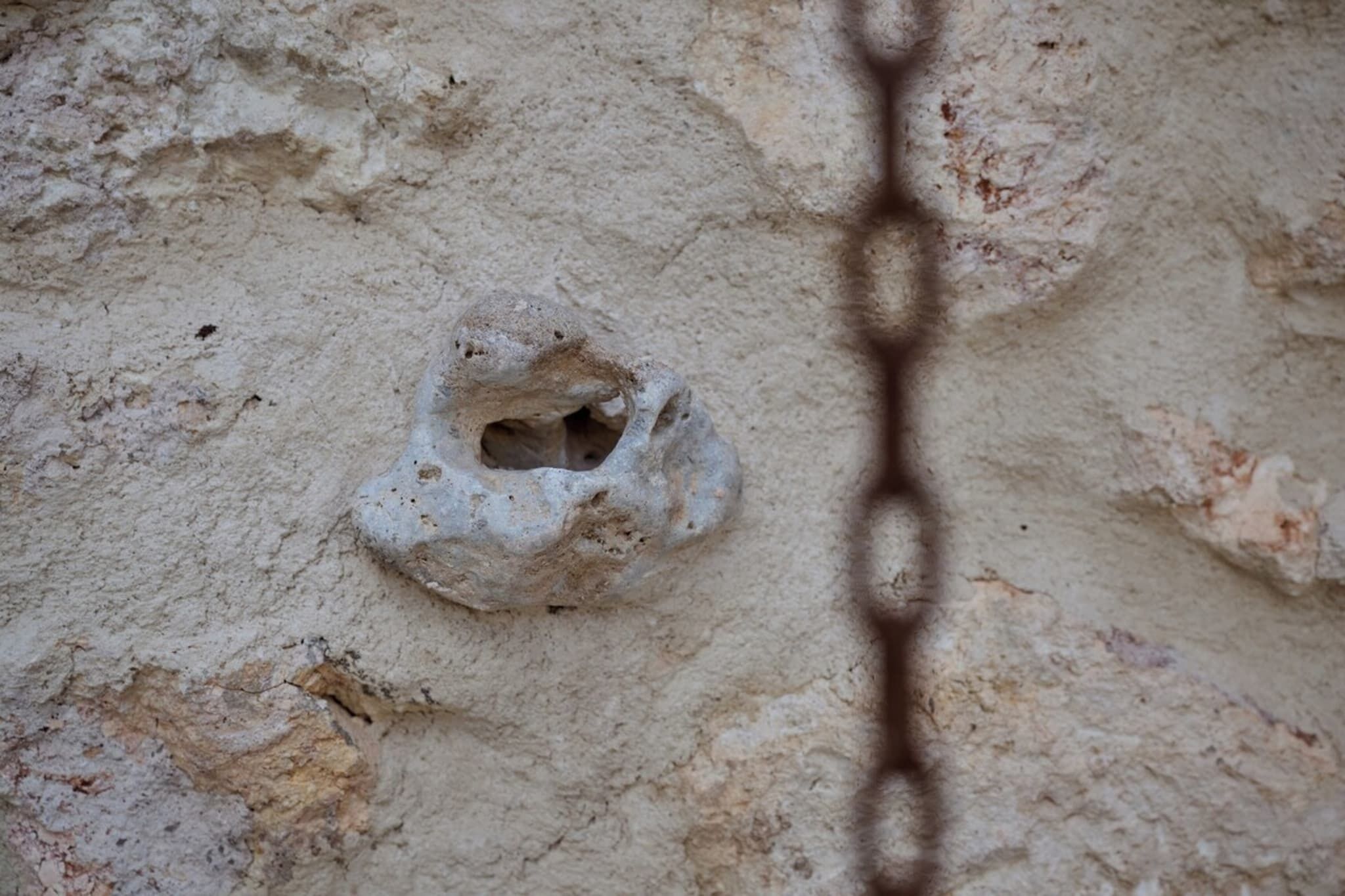 A rough, textured wall with a circular hole and a chain.
