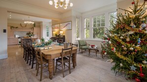 A spacious dining area with a wooden table and chairs, a Christmas tree, and a view of the kitchen and dining room. - Windy Ridge - sleeps 16 guests  in 6 bedrooms (Bembridge)