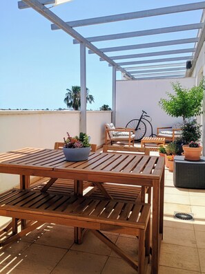 Un espace extérieur aménagé en bois, avec des tables et des chaises, un vélo et des plantes en pot.