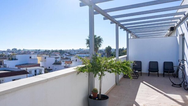 A rooftop terrace with a pergola, potted plants, and outdoor seating.