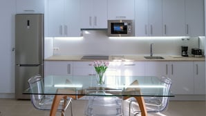 A modern kitchen with white cabinets, stainless steel appliances, and a glass dining table with chairs.