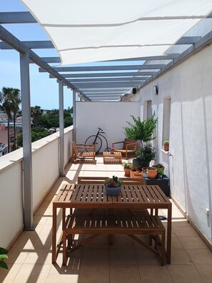 Un espace extérieur aménagé, abrité et doté de mobilier en bois et de plantes en pot.