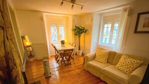Un salon avec un plancher en bois, une table à manger avec des chaises, un canapé avec des coussins à motifs et une plante en pot.