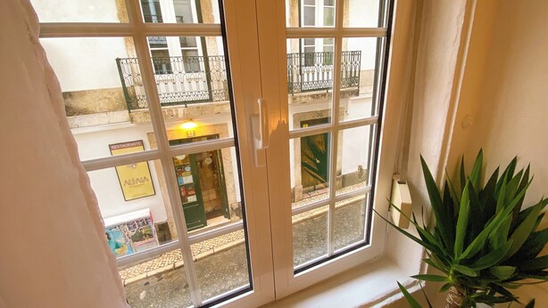Une fenêtre donnant sur un immeuble doté de balcons et d’une enseigne indiquant « RESTAURANT ».