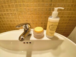 Ein Badezimmerwaschbecken mit einem Chromarmaturen-Set, einer Seifenspender und einer Flasche Flüssigseife.