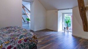 A bedroom with a bed, wooden flooring, a skylight, and a view of a balcony with plants.