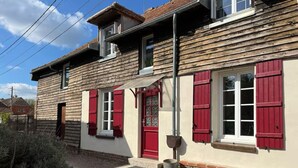 A two-story building with red shutters, a visible window, and a small porch area.