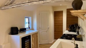 A compact kitchen with a built-in oven, a coffee machine, and a rustic wooden ceiling.